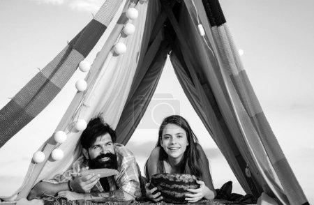 Téléchargez les photos : Couple romantique manger pastèque dans la tente sur le camping. Aventure en plein air avec des amis sur la nature. Aliments biologiques - en image libre de droit