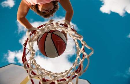 Photo for View of flying ball to basket from top, kid play basketball. Little child boy playing basketball with basket ball. Active kids lifestyle - Royalty Free Image