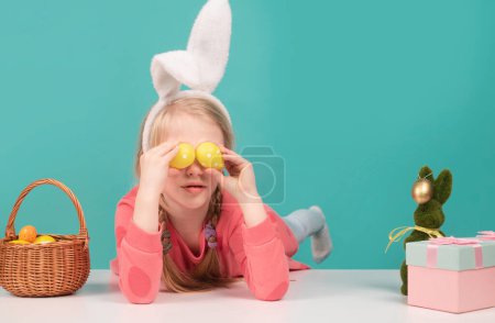 Foto de Lindo niño pequeño con orejas de conejo en el día de Pascua. Chica sosteniendo huevos pintados en los ojos - Imagen libre de derechos