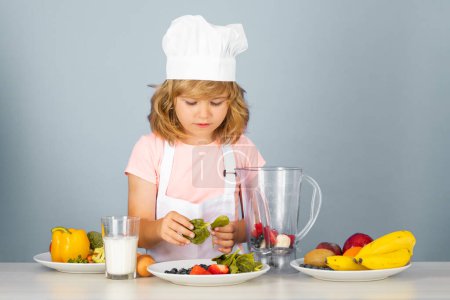 Photo for Child chef cook prepares food on isolated grey studio background. Kids cooking. Teen boy with apron and chef hat preparing a healthy vegetables meal in the kitchen - Royalty Free Image