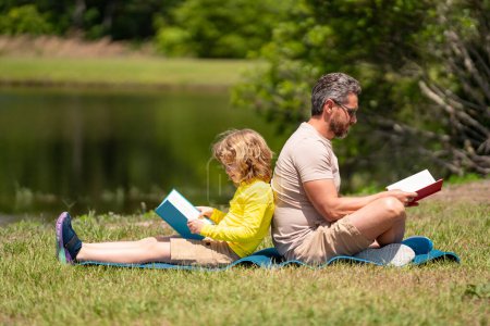 Photo for Father and son reading book in park, man encourages boy to knowledge, family education. Father and child read book together outdoor. Happy parent reading with child book on summer nature in park - Royalty Free Image