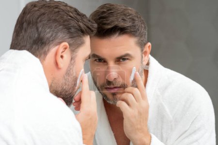 Photo for Beauty man applying cream on skin face. Handsome serious man enjoy fresh perfect skin, applying facial cream. Portrait of man with cosmetic cream on face skin. Facial treatment. Male beauty face - Royalty Free Image