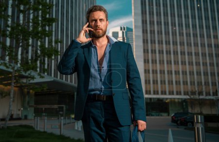 Photo for Caucasian business man in suit comes out office talking on phone. concept of end working day. Sexy fashion businessman - Royalty Free Image