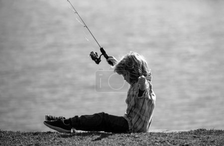 Foto de Pesca infantil. Joven pescador. Chico con spinner en el río. Retrato de chico interesado pescando en embarcadero con caña en el lago. Concepto de pesca - Imagen libre de derechos