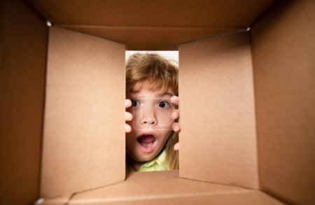 Photo for Kid opening package. Child boy age 6 year opening a carton box and looking inside, unpacking concept, surprise unboxing - Royalty Free Image