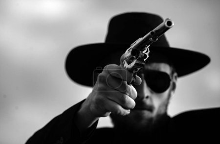 Photo for Cowboy shooter in black suit and cowboy hat. Serious man with wild west guns, retro pistol revolver and marshal ammunition. American western Sheriff. Wild west wanted concept - Royalty Free Image