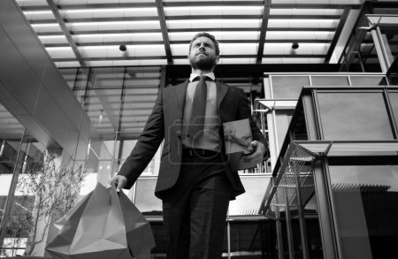 Téléchargez les photos : Homme d'affaires portant des sacs à provisions, marchant en ville - en image libre de droit