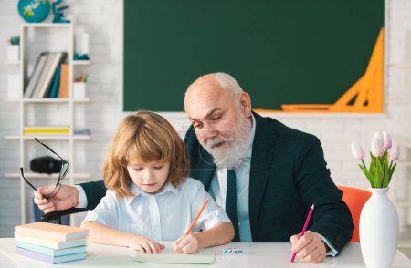 Photo for Old teacher and young schoolboy doing homework assignment at school. Teachers day - Royalty Free Image