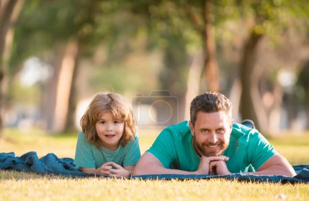 Téléchargez les photos : Père et fils couchés sur l'herbe dans le parc d'été passer du temps en plein air ensemble - en image libre de droit
