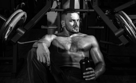 Photo for Fit man. Young muscular man with naked torso working out in gym. Resting time. Tired sporty man resting after training. Man with bottle of water or protein - Royalty Free Image