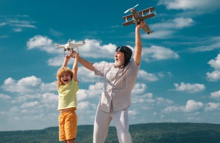 Téléchargez les photos : Grand-père et fils avec avion et drone quadcopter sur fond bleu ciel et nuages. Aîné parent âgé avec enfant - en image libre de droit