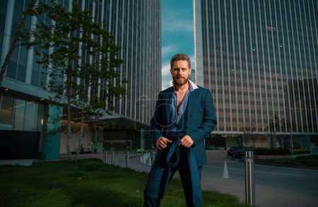 Téléchargez les photos : Homme d'affaires sexy moderne en costume de mode debout à l'extérieur avec paysage urbain - en image libre de droit
