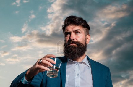 Photo for Man with beard holds glass brandy, drink cognac. Guy hipster tastes drink. Sipping whiskey. Luxury nightlife, rich bearded man drink expensive beverage - Royalty Free Image