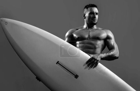Téléchargez les photos : Un type sur la plage avec une planche de surf. Jeune surfeur tenant une planche de serf. Concept vacances d'été. Surfeur musclé sexy avec une planche de surf. Garçon d'été, isolé sur bleu - en image libre de droit