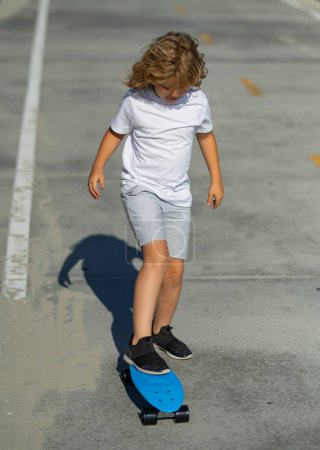 Téléchargez les photos : Enfant skateboarder tour sur skateboard dans le parc. Jeune adolescent souriant chevauchant sur un skateboard de croisière moderne, fond urbain - en image libre de droit