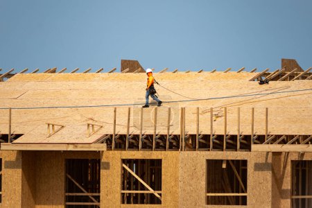 Téléchargez les photos : Constructeur de toiture sur le toit sur le chantier de construction. Travailleur sur le toit. Toit sur le lieu de travail élevé. Travailleurs sur les chantiers de construction toiture. Travaux de toiture. Outils de toiture pour toitures en bois - en image libre de droit