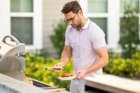 Photo for Male chef grilling and barbequing in garden. Barbecue outdoor garden party. Handsome man preparing barbecue meat. Concept of eating and cooking outdoor during summer time - Royalty Free Image