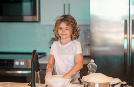 Téléchargez les photos : Enfant garçon laver la vaisselle dans l'évier de la cuisine. Nettoyer la vaisselle, le liquide vaisselle avec de la mousse - en image libre de droit