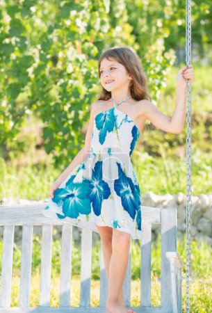 Photo for Fashion kids dress. Child playing on swing. Healthy summer activity for children in warm weather. Little kids swinging. Cute little girl having fun on a swing in beautiful summer garden outdoors - Royalty Free Image