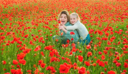 Foto de Hermosa madre e hija en el campo de flores de amapola de primavera. Mamá sostiene a su hija en el paseo a cuestas del prado floreciente. Feliz maternidad. - Imagen libre de derechos