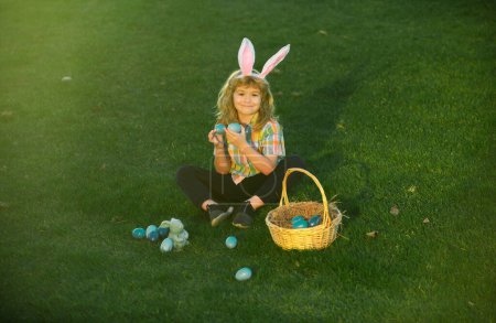 Téléchargez les photos : Des lapins avec des oreilles de lapin. Chasse aux œufs de Pâques dans le jardin. Enfant garçon jouant dans le champ, chassant des œufs de Pâques - en image libre de droit
