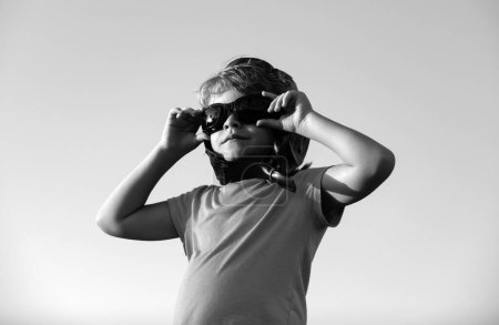 Téléchargez les photos : Enfant garçon jouant avec des lunettes de pilote et un casque, rêve de devenir pilote. Rêves d'enfants. Enfant pilote aviateur sur ciel - en image libre de droit