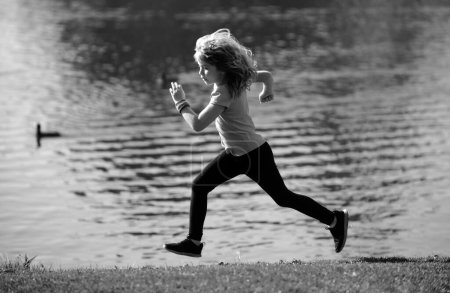 Foto de Niños corriendo o corriendo cerca del lago en el césped en el parque. Corredor de chicos corriendo en el parque al aire libre. Correr es un deporte que fortalece el cuerpo. Deportes al aire libre y fitness para niños, ejercicio al aire libre - Imagen libre de derechos