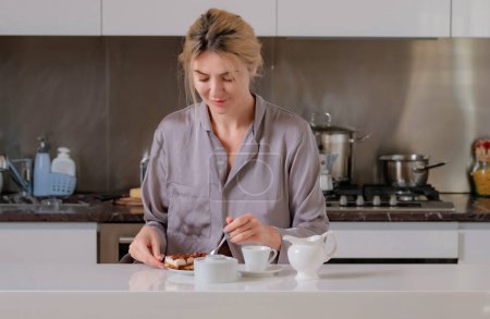 Téléchargez les photos : Une femme boit du café dans la cuisine. Fille en pyjama relaxant dans la cuisine de la maison. Jeune femme au foyer dans préparer le café dans la cuisine - en image libre de droit