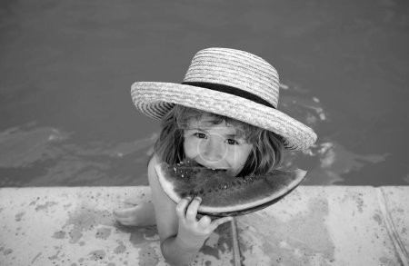 Téléchargez les photos : Un drôle d'enfant joue dans la piscine. L'enfant mange une pastèque sucrée, profiter de l'été. Enfance insouciante - en image libre de droit