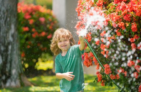 Foto de Niños regando flores y plantas en el jardín. Niño con manguera de agua en el patio trasero. Jardinería para niños. Niños verano diversión al aire libre en casa - Imagen libre de derechos