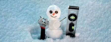 Téléchargez les photos : Bonhomme de neige réparateur avec des outils de réparation. Soutien réparation et récupérer le service. Bonhomme de neige sur fond de neige - en image libre de droit