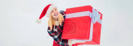 Téléchargez les photos : Service de livraison d'hiver. Femme portant un grand cadeau isolé sur fond d'hiver de neige. Portrait de Santa femme avec un énorme cadeau rouge - en image libre de droit