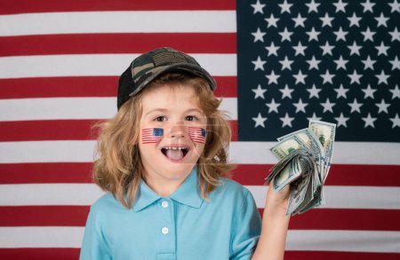 Téléchargez les photos : L'argent américain. Portrait d'enfant avec billets de banque. Enfant avec de l'argent. Les enfants apprennent la responsabilité financière de l'épargne. Drapeau américain sur la joue de l'enfant. Portrait d'enfant américain - en image libre de droit
