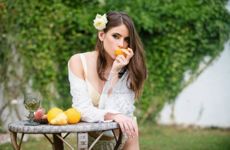 Photo for Young woman with fresh fruit on a wooden table in garden outdoors eating orange. Healthy vegetarian food, healthcare. Sexy young woman eating orange fruits. Sexy woman squeezing juice from fresh - Royalty Free Image