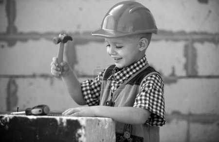 Téléchargez les photos : Enfant en casque dur tenant le marteau. Petit enfant aidant avec des outils de jouet sur le site construciton. Des enfants avec des outils de construction. Travailleur de la construction. Constructeur et réparation d'enfants - en image libre de droit