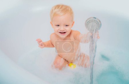 Photo for Small little cute sweet blonde boy bathes in a bath with foam and soap bubbles. Adorable little boy have fun time with bubble bath - Royalty Free Image