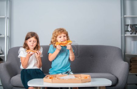Photo for Happy daughter and son eating pizza. Children kids enjoy and having fun with lunch together at home. Two young children bite pizza indoors - Royalty Free Image