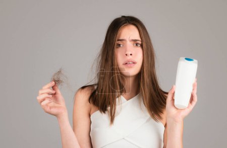 Photo for Hair loss. Woman with bootle shampoo is upset of hair loss. Portrait of sad girl with problem hair, isolated. Worried girl holding long damaged unhealthy hair in hand - Royalty Free Image