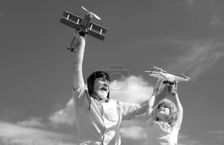Photo for Old grandfather and young child grandson with toy jetpack plane and quadcopter drone against sky. Child pilot aviator with plane dreams of traveling - Royalty Free Image