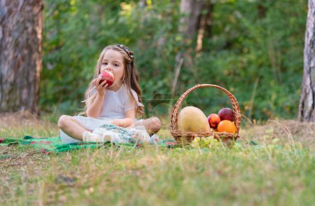 Foto de Picnic en el bosque para niños. Niño con cesta de frutas de otoño comiendo manzana. Niño pequeño en Sunny Park. Niña disfrutando de ocio otoño - Imagen libre de derechos