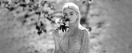 Foto de Retrato al aire libre de una joven hermosa mujer de moda posando cerca del árbol de sakura floreciente. Diseño de primavera para encabezado de banner o sitio web, espacio de copia - Imagen libre de derechos