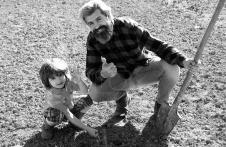 Foto de Padre plantando con su hijo ayudante. Papá y los niños de jardinería en el jardín. Cultivando plantas. Concepto de cosecha primavera - Imagen libre de derechos