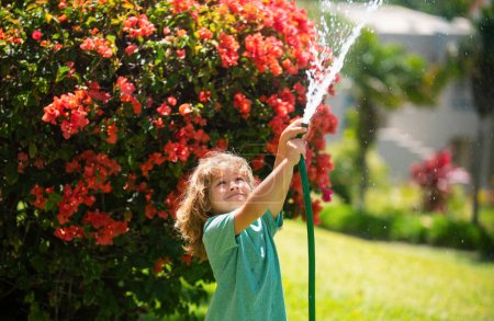 Photo for Funny kid have fun and happy smiling on nature backyard. Watering plants in the garden at home on summer day - Royalty Free Image