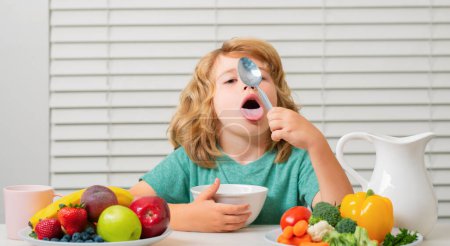 Foto de Kid bot lamer cuchara comiendo comida. Nutrición saludable para los niños. Los niños disfrutan desayunando o cenando con apetito. Niño hambriento come frutas y verduras sabrosas - Imagen libre de derechos