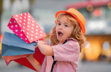 Photo for Excited kid in fashion clothes goes shopping. Amazed kid with shopping packages outdoor. Shopper child with shopping bag walking on street and carrying shopping bags - Royalty Free Image