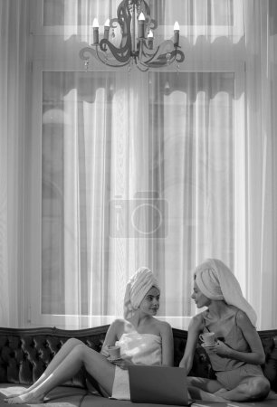 Téléchargez les photos : Happy young women wearing bathrobes and towel on heads celebrating wedding or birthday party, sitting on bed - en image libre de droit