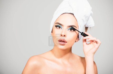 Photo for Woman applying black mascara on eyelashes with makeup brush. Brows coloring, wax and lamination. Beauty portrait of girl with towel on head and make up - Royalty Free Image