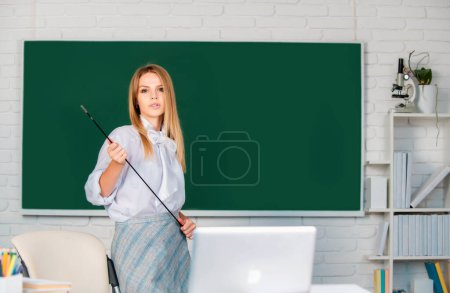 Photo for Young teacher with pointer on blackboard with copy space. Beautiful student, cute blonde young woman in class at school - Royalty Free Image
