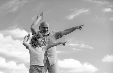 Téléchargez les photos : Jeune petit-fils et vieux grand-père jouant avec jouet avion en papier sur fond de ciel d'été - en image libre de droit