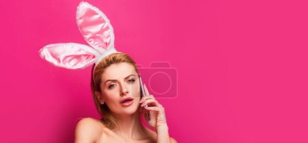 Foto de Banner de Pascua con mujer conejita. Mujer de Pascua con orejas de conejo hablando por teléfono, aislado en rosa - Imagen libre de derechos